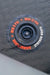 A close-up of a circular black air mat valve assembly with red and white text reading 'MIN 6 PSI', 'MAX 12 PSI', 'AIRMAT FLOOR', and 'STRYKER BOATS', set against a dark textured mat surface.