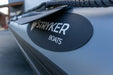 Close-up of a gray boat hull with a black oval sticker reading STRYKER BOATS in white text, plus part of a dark rope and blurred outdoor background.